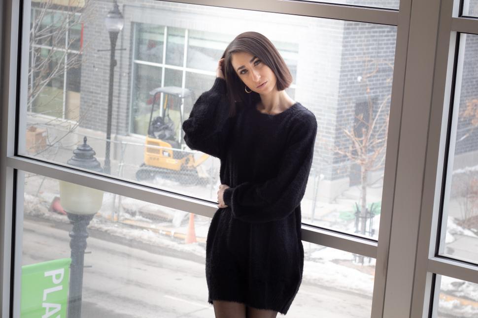 Free Image of Woman in black sweater standing by window inside building 
