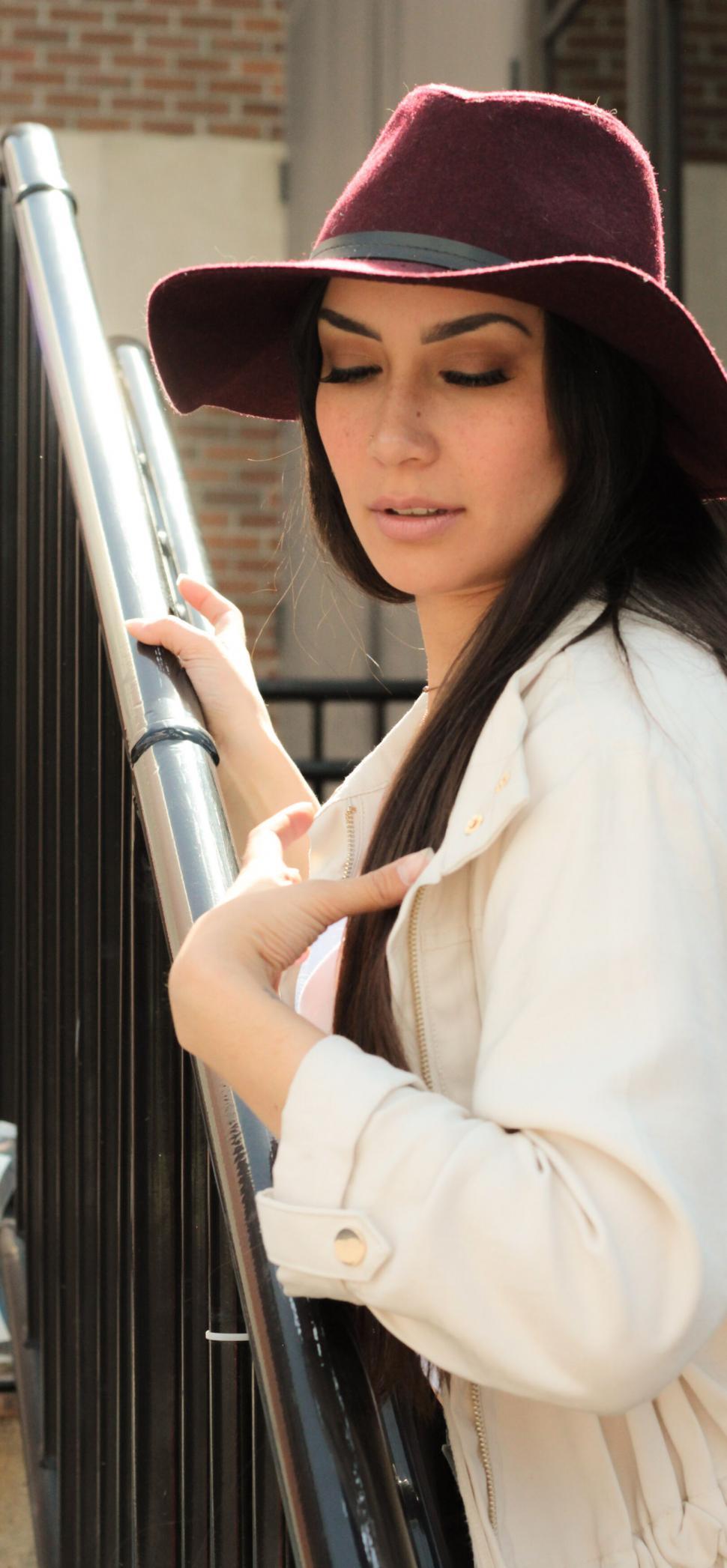 Free Image of Woman in maroon hat and beige jacket by black railing 