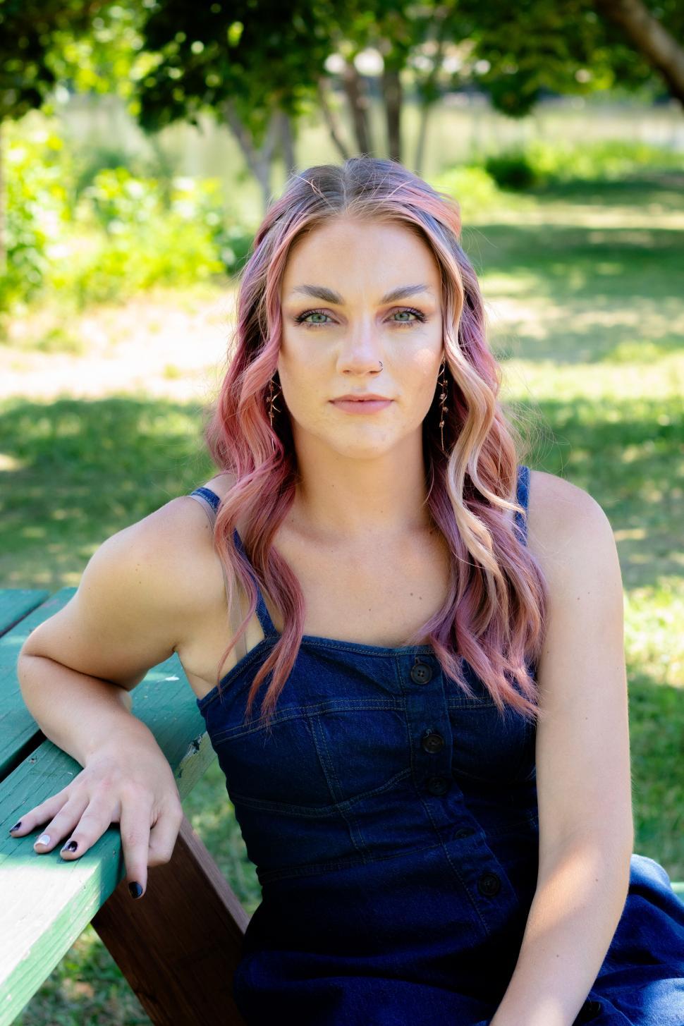 Free Image of Woman with pink hair sitting by wooden park table. 