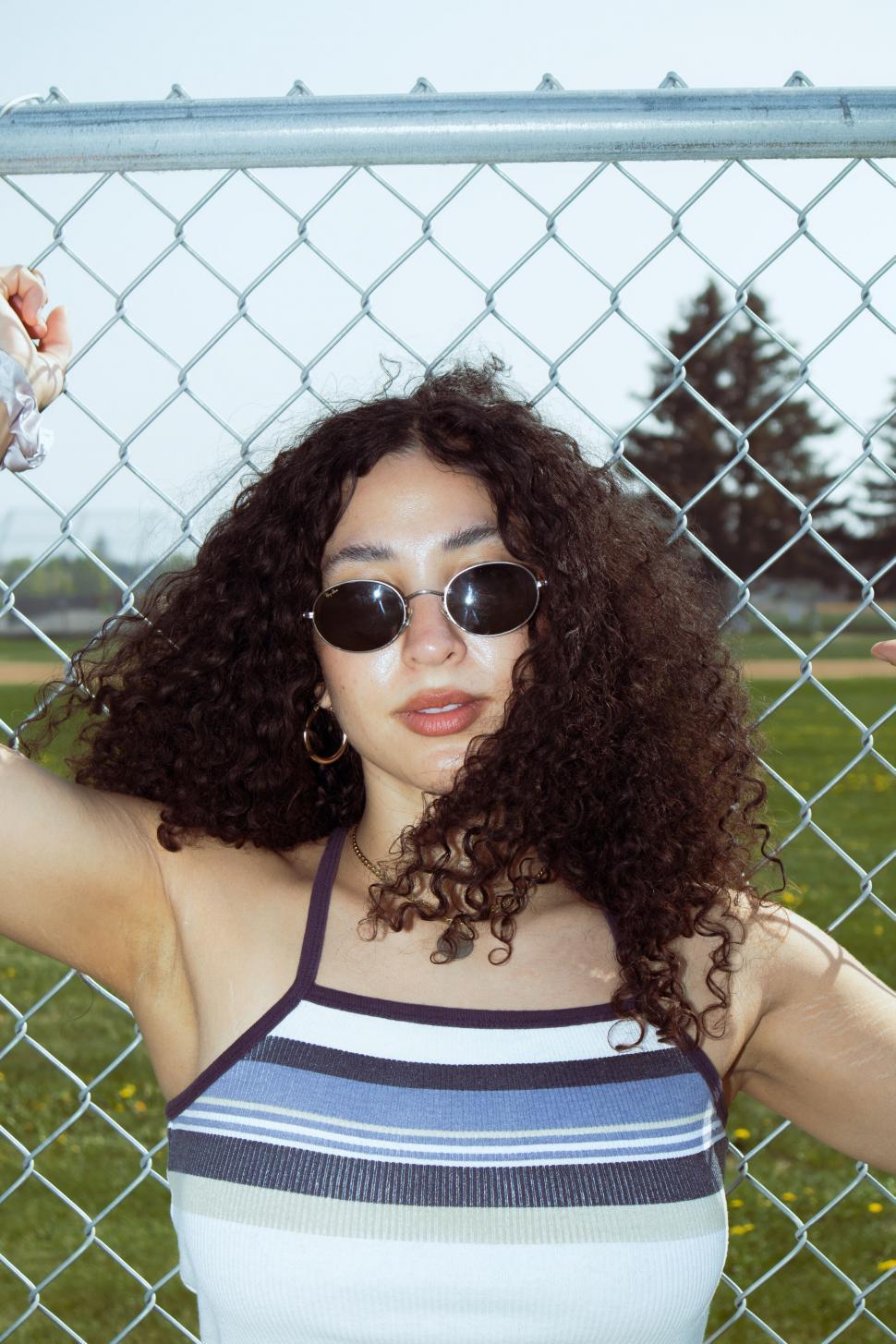 Free Image of Woman with curly hair standing against fence in sunlight 