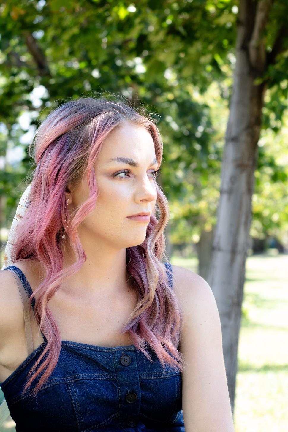 Free Image of Woman with pink hair sitting outdoors looking thoughtful 