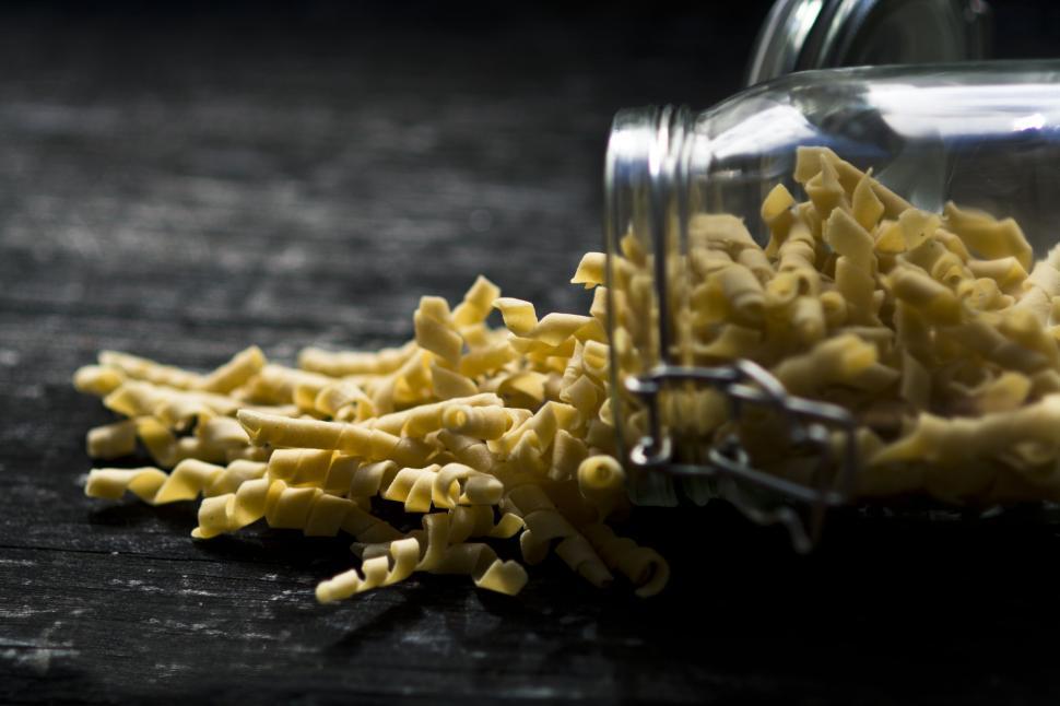Free Image of Scattered noodles on dark surface from a glass jar. 