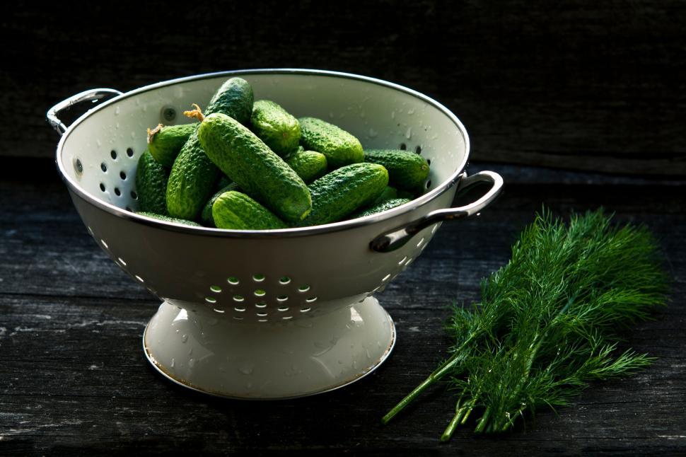 Free Image of Green cucumbers in a white colander next to fresh dill. 