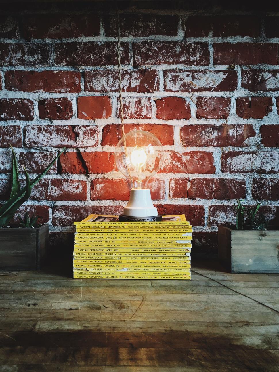 Free Image of Bright light bulb atop stacked yellow magazines 