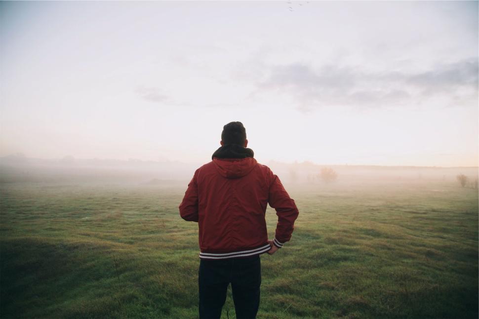 Free Image of Lone person in red jacket standing in open misty field 