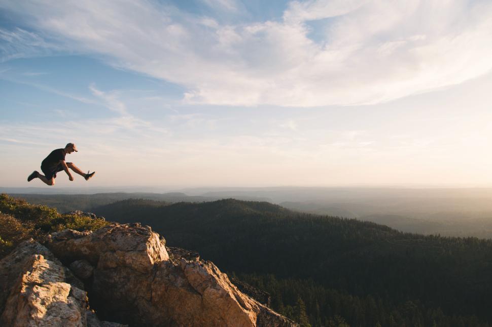 Free Image of Person jumping at the edge of rocky cliff above forest 
