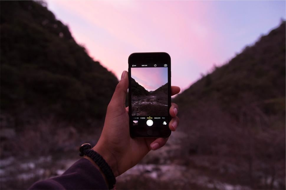 Free Image of Hand holding phone capturing a picturesque mountain view 