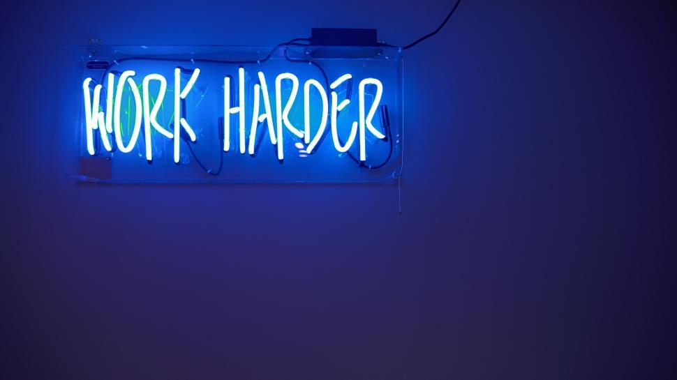 Free Image of Blue neon sign with glowing text  WORK HARDER , wall 