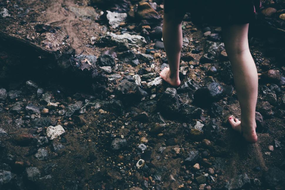 Free Image of Barefoot walking on rocky terrain near a stream. 