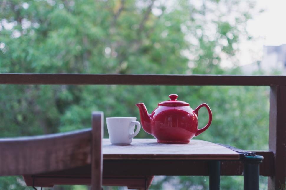 Free Image of Red teapot and white cup on a rustic outdoor table. 