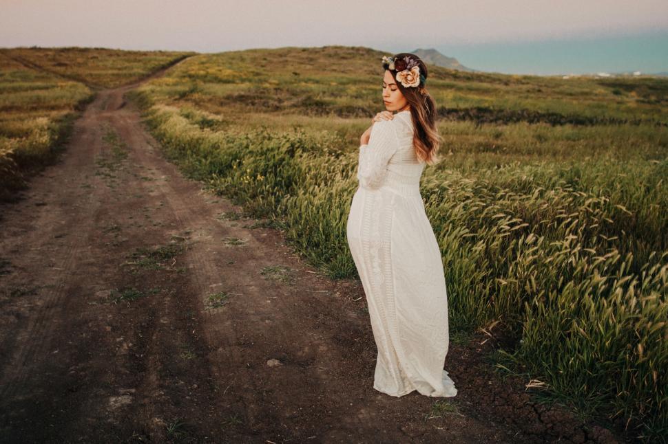 Free Image of Woman standing on a dirt road in an open field 