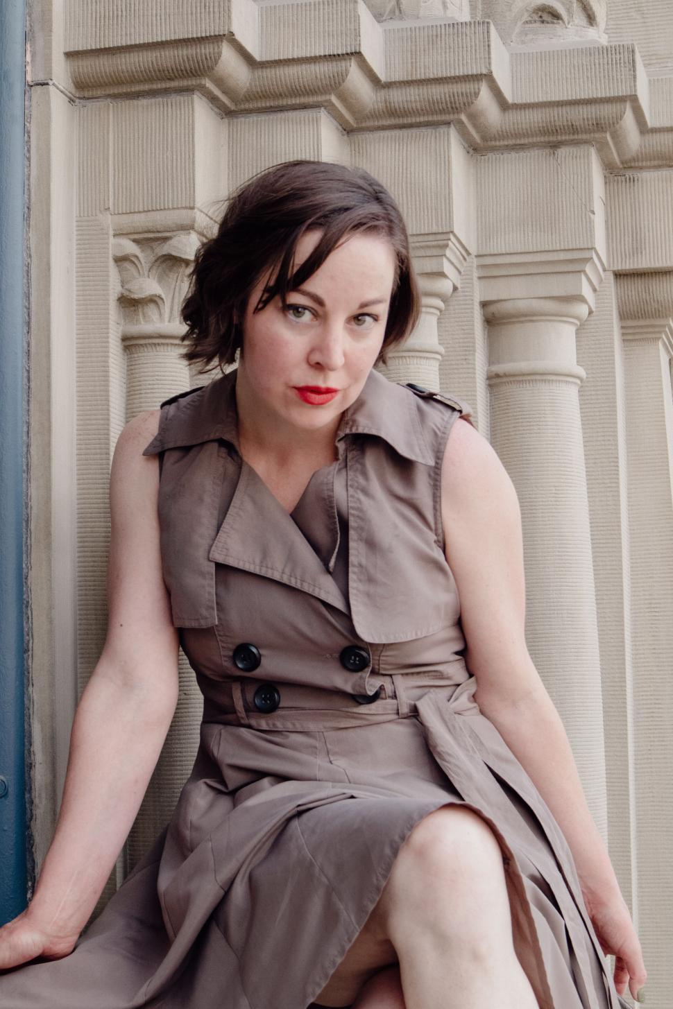 Free Image of Woman in trench coat sitting on steps of ornate building 