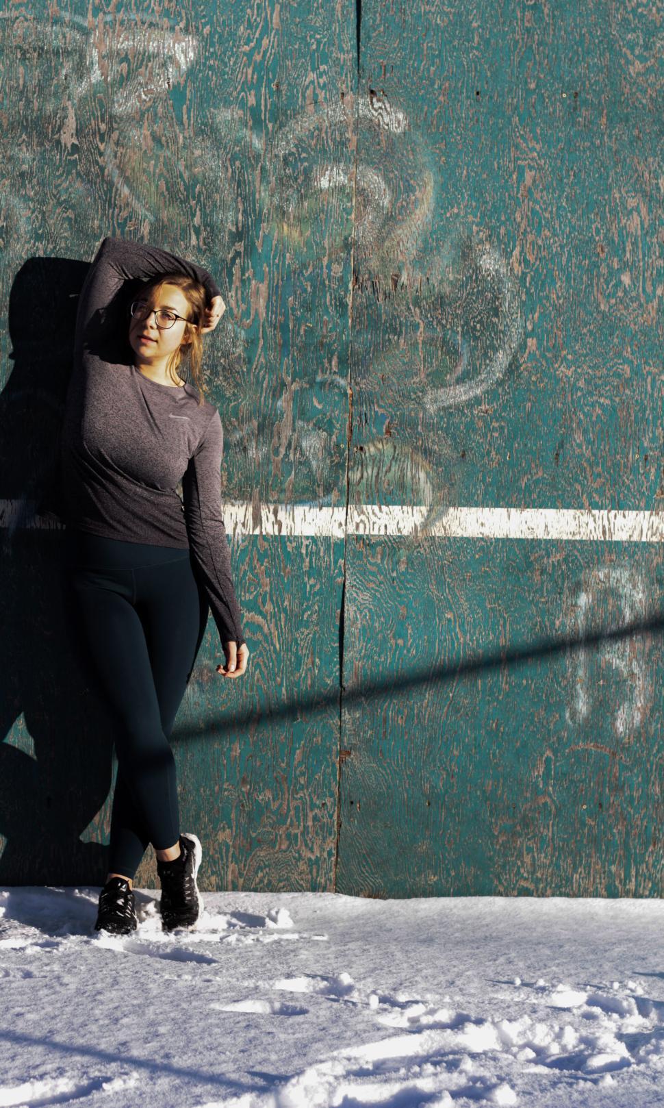 Free Image of Woman standing against weathered wall in cold outdoor setting 