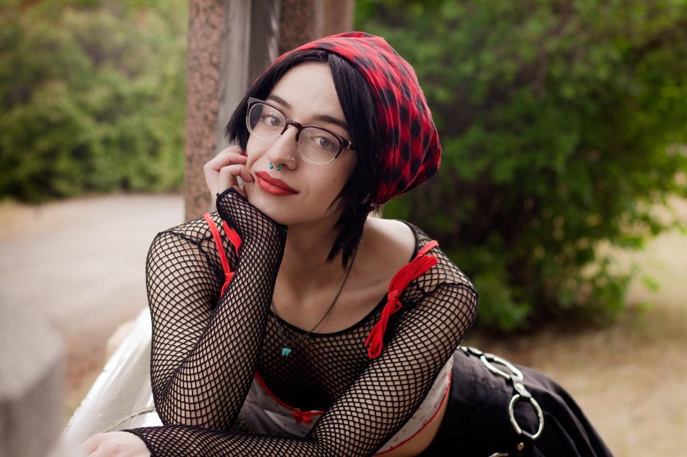 Free Image of Woman in artistic outfit with piercings leaning on fence 