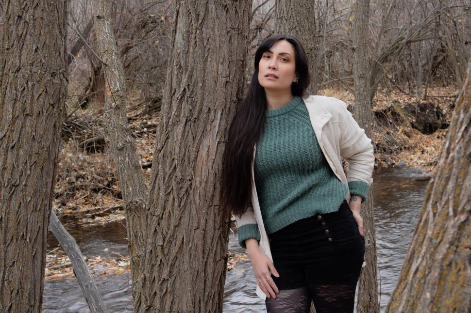 Free Image of Woman in white jacket standing among trees near a stream 