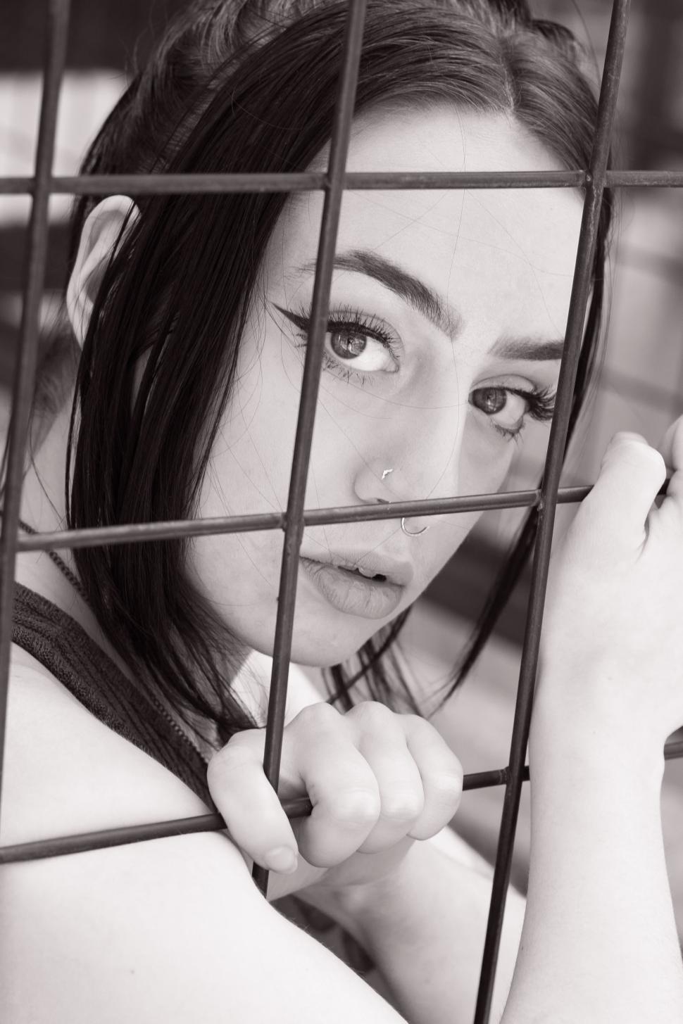 Free Image of Woman looking through bars with a thoughtful expression. 