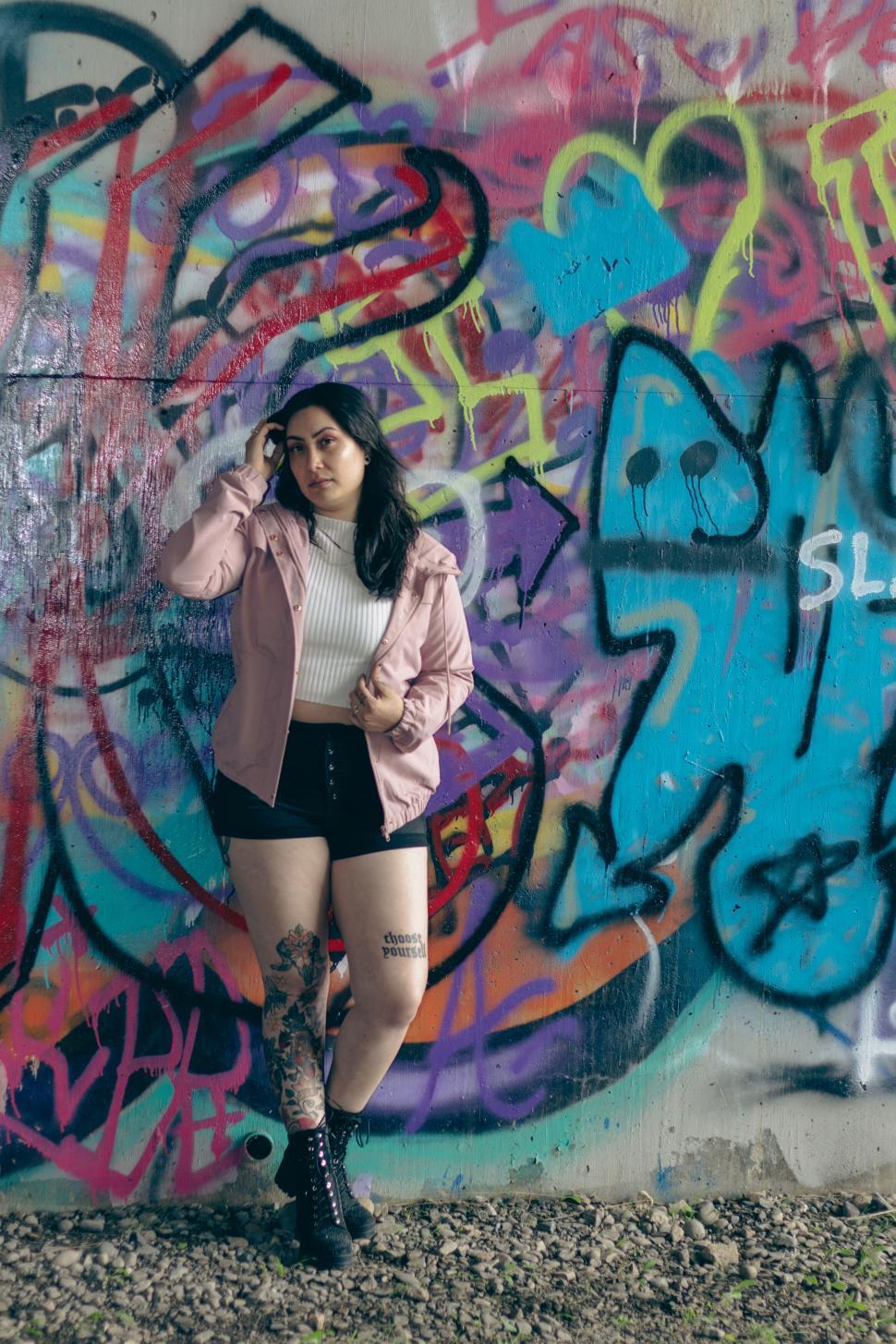 Free Image of Woman posing in front of colorful graffiti wall art 