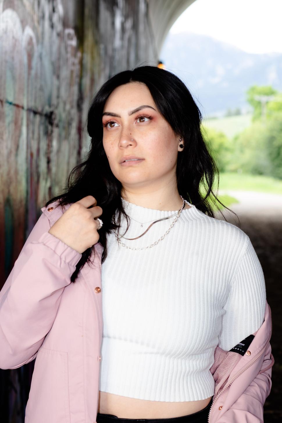 Free Image of Young woman posing under bridge with graffiti background 