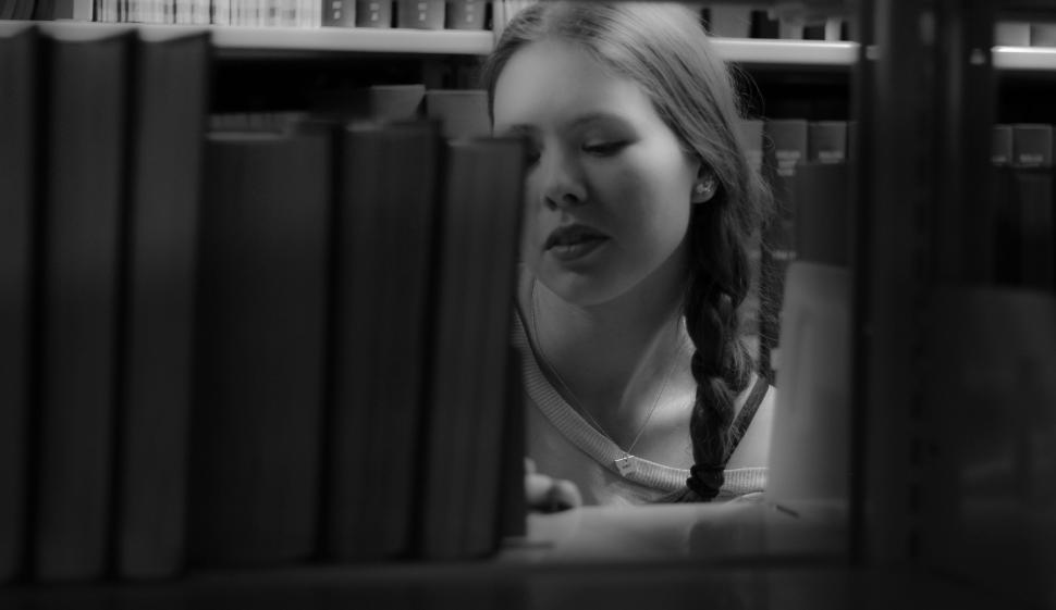 Free Image of Woman with braid searching books in a dimly lit library 