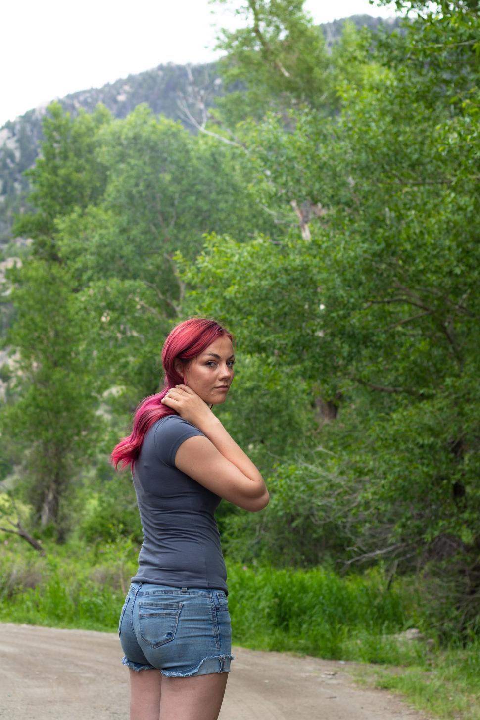 Free Image of Woman with pink hair in nature, grey shirt, and shorts 