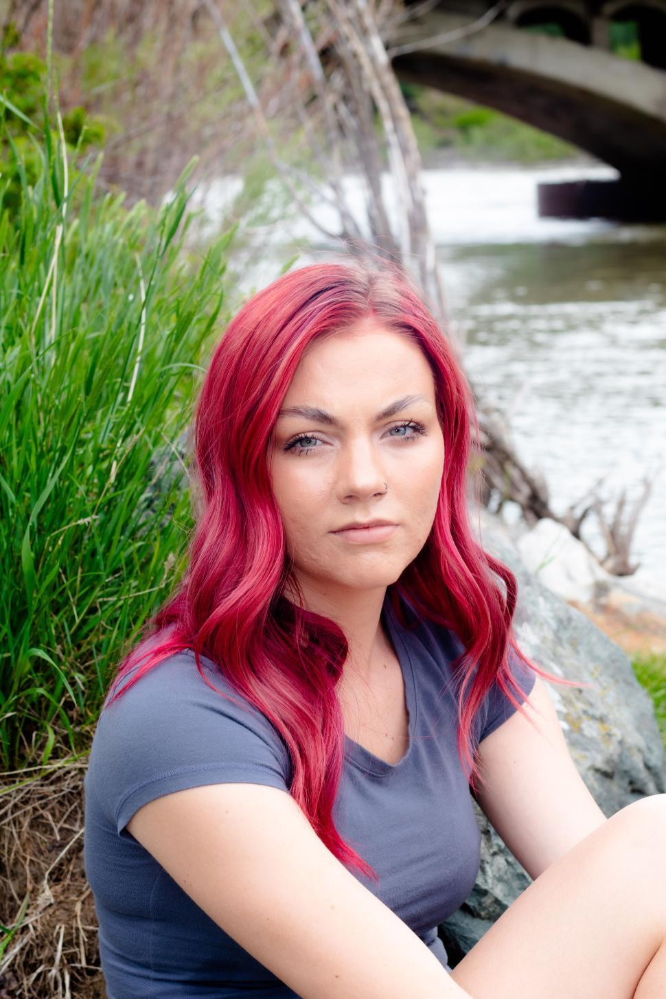 Free Image of Young woman with red hair sitting by a river bank 