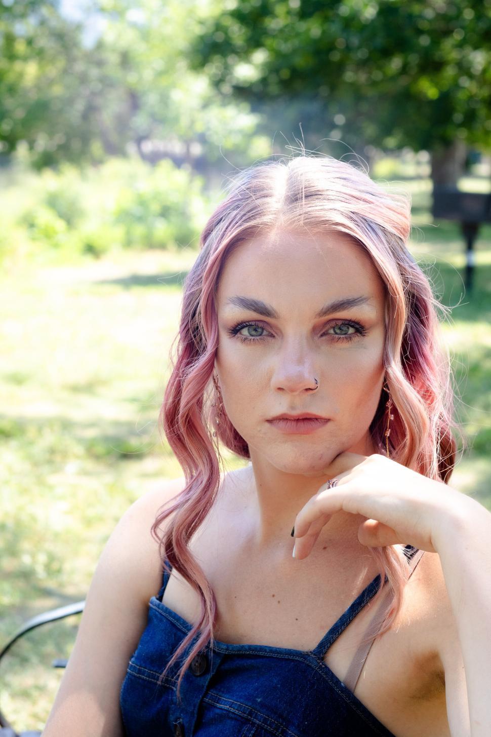 Free Image of Young woman with pink hair sitting outdoors in summer. 