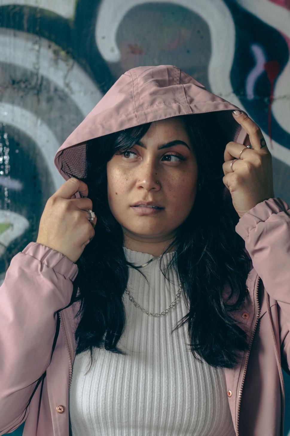 Free Image of Person in pink hoodie standing against graffiti wall 