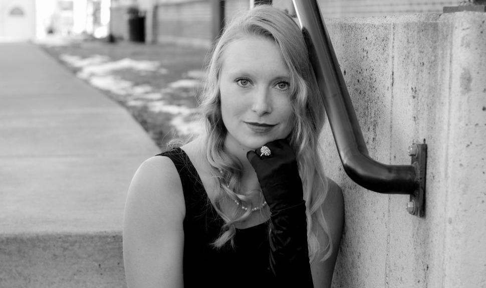 Free Image of Blonde woman in black dress sitting next to a concrete wall 