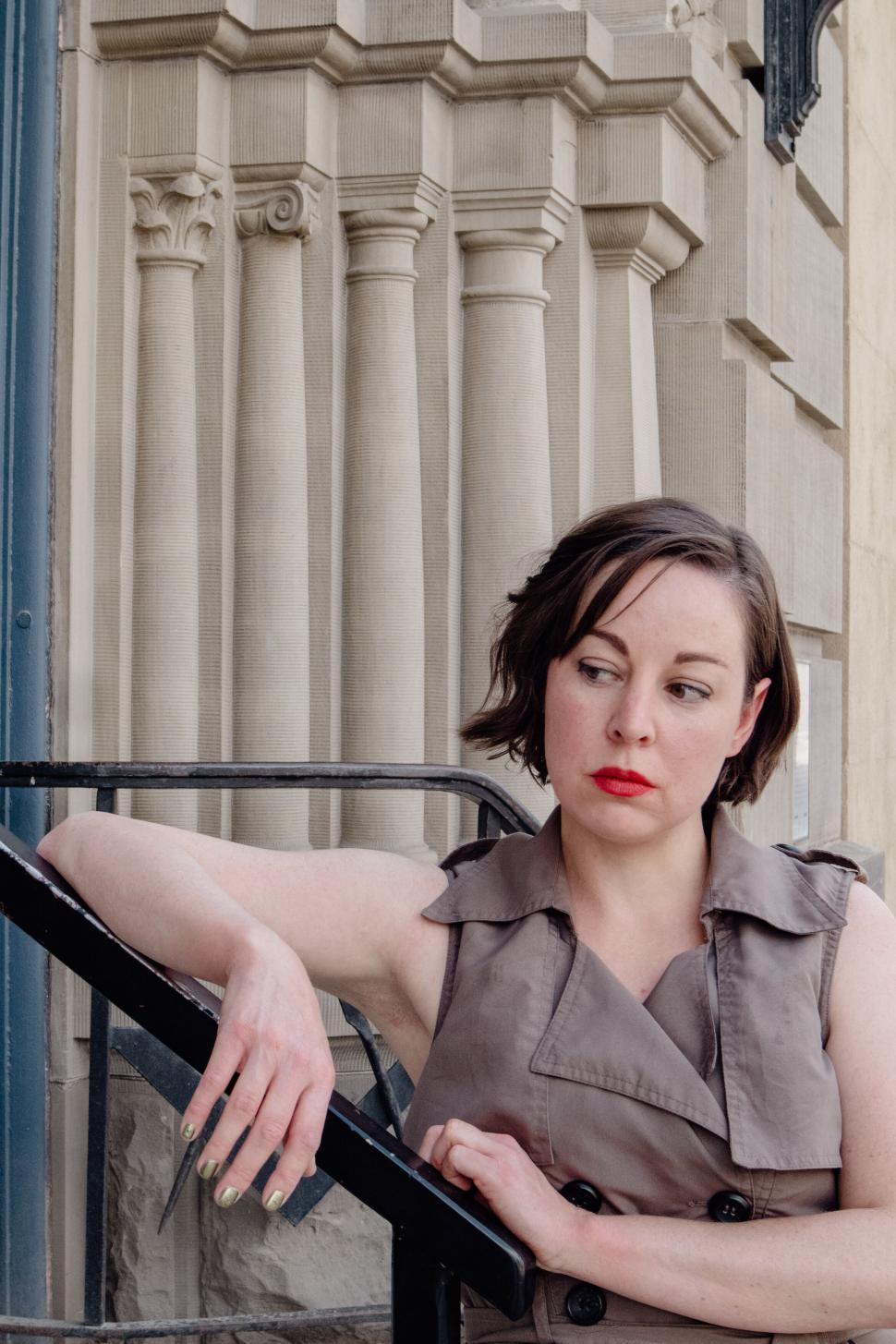 Free Image of Woman in sleeveless jacket leaning on stairs outdoors 