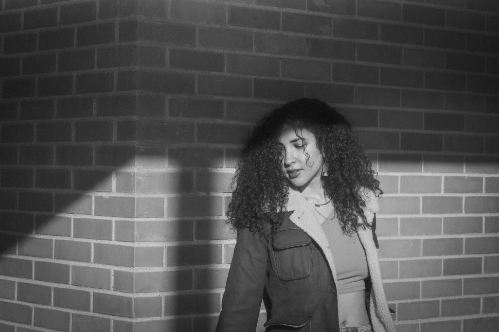Free Image of Person with curly hair standing by brick corner wall. 