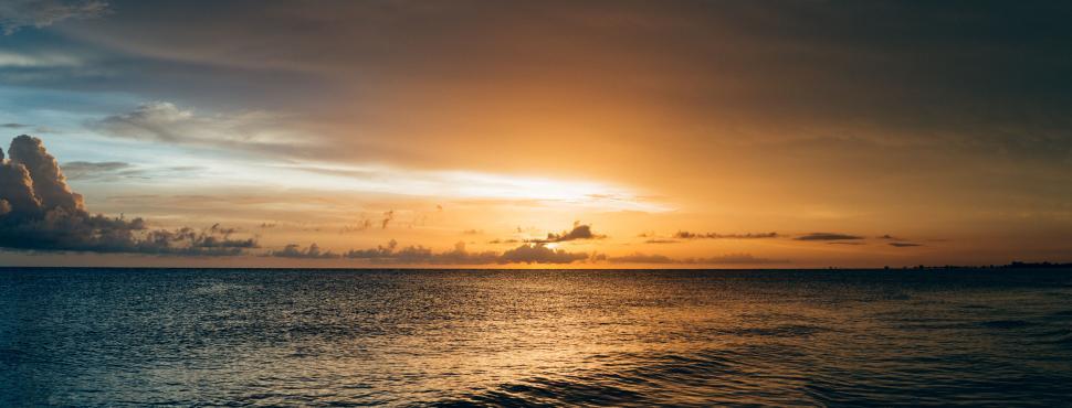 Free Image of Golden sunset over the sea with calm waves and clouds. 
