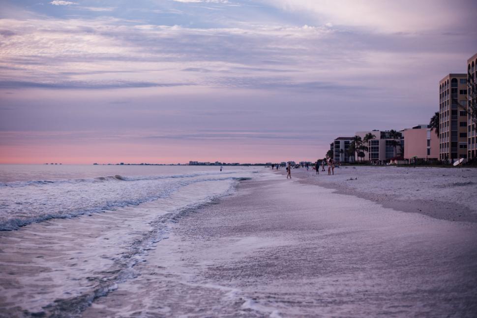 Free Image of Peaceful beach with gentle waves and distant buildings. 