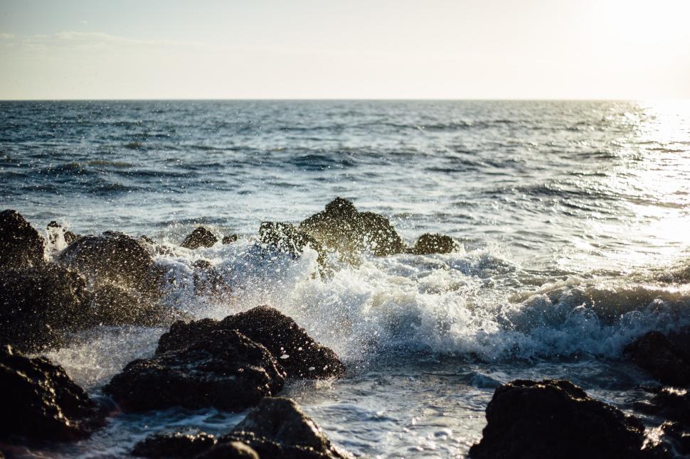 Free Image of Waves crashing against rocks along a sunny coastline. 