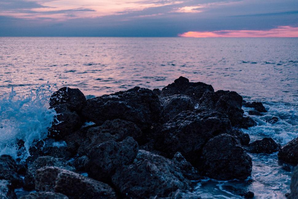 Free Image of Waves crashing against rugged rocks at dramatic dusk. 