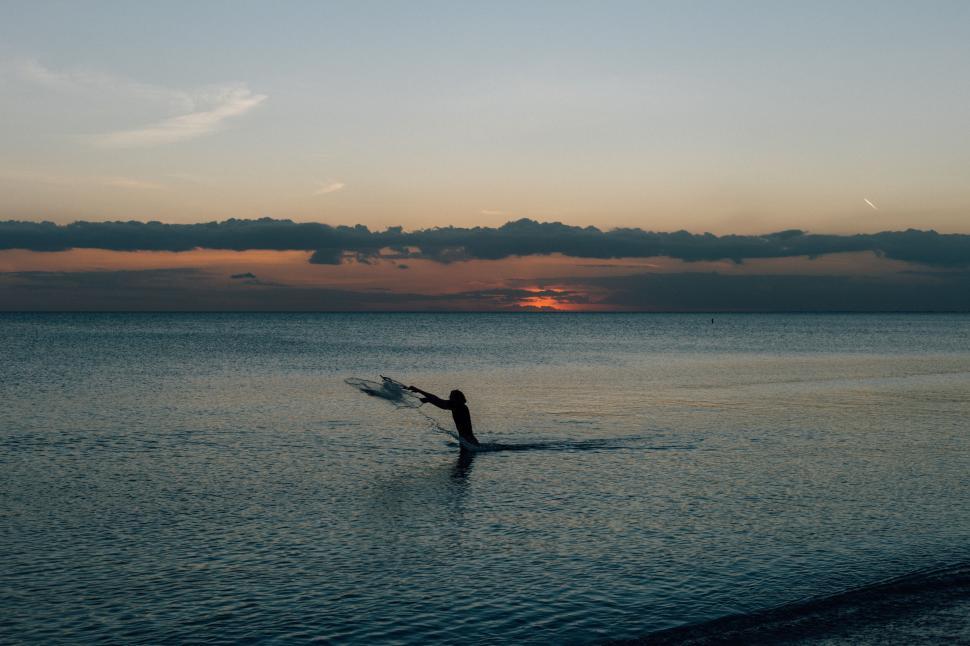 Free Image of Person casting fishing net in calm ocean at early dusk. 