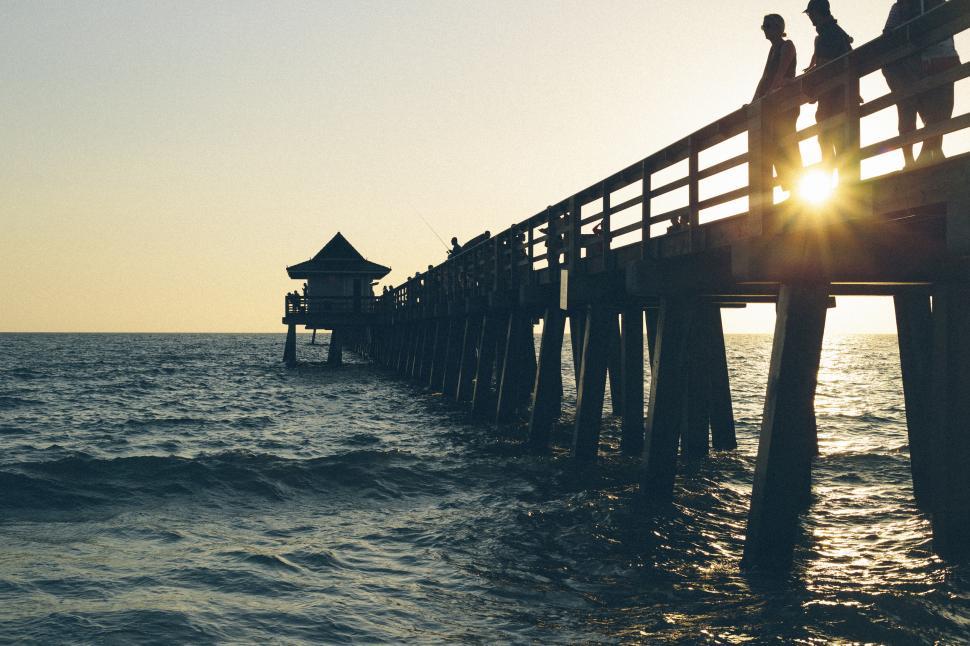 Free Image of Silhouette of pier with people at sunset, serene ambiance 