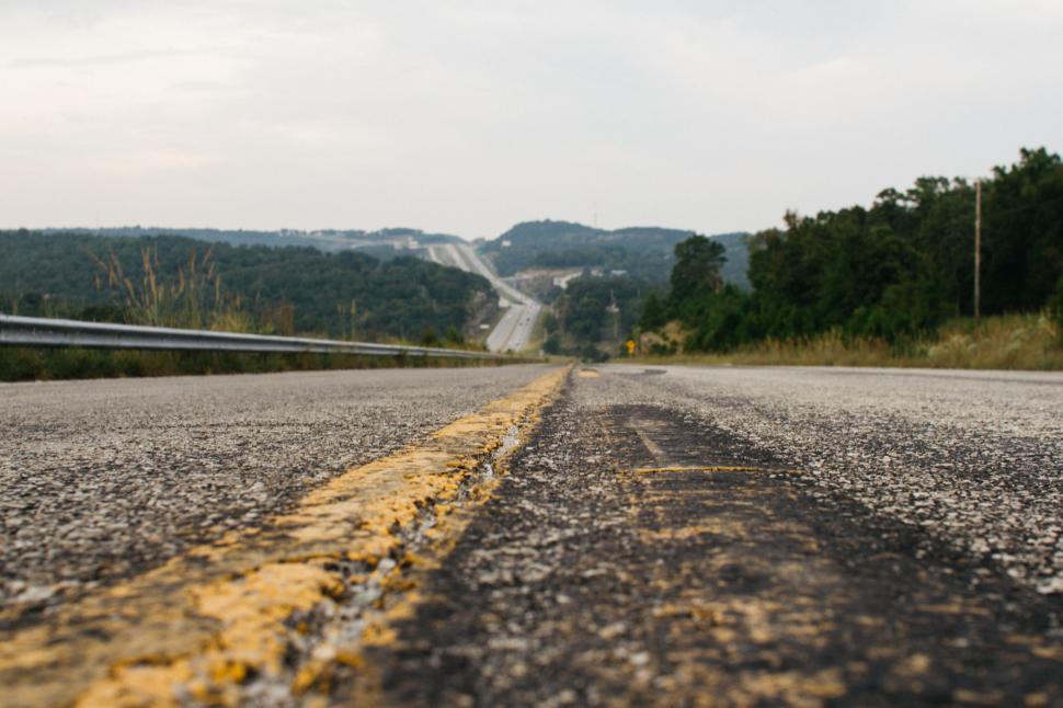 Free Image of Roadway extending into hilly terrain, green surroundings 