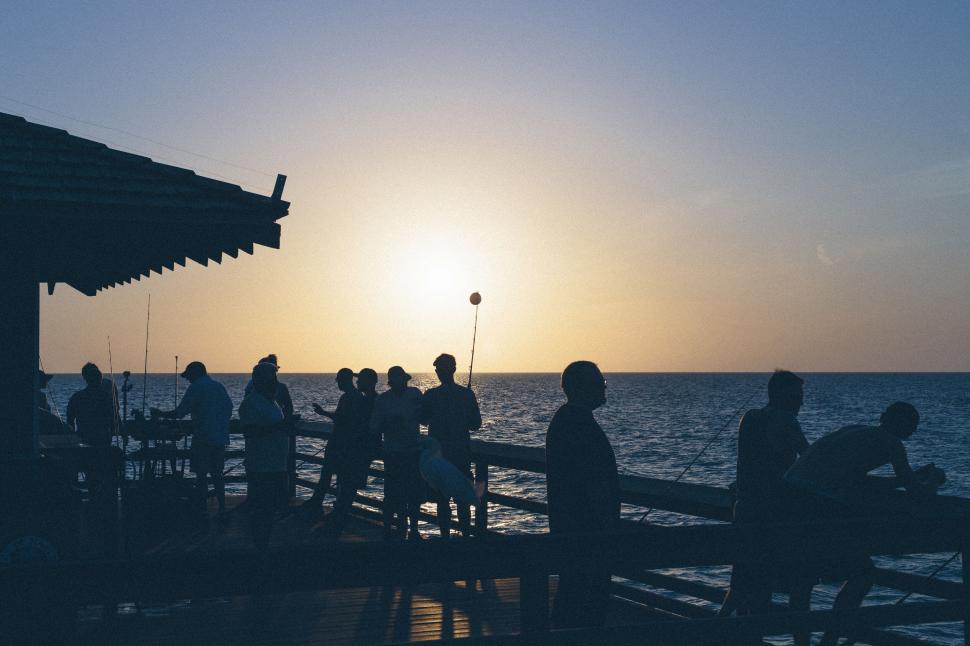 Free Image of Silhouette of people fishing off a pier at sunset time. 