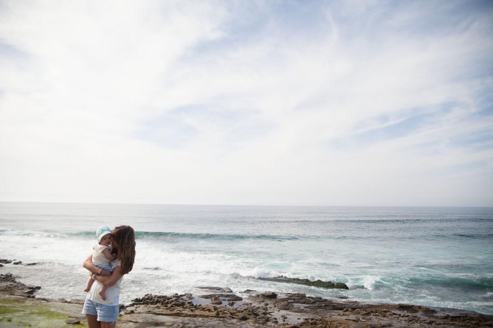 Free Image of Mother holding child at beach with waves in background 