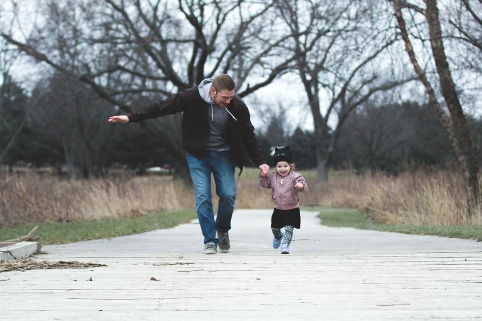 Free Image of Adult guiding child on a park pathway with bare trees 