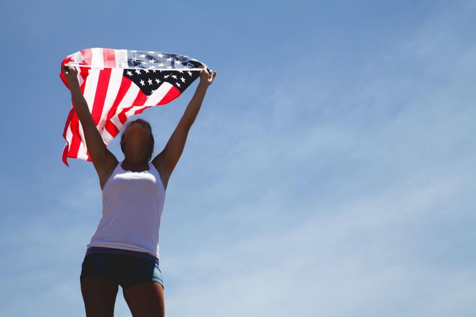 Free Image of Person holding American flag upwards against blue sky. 