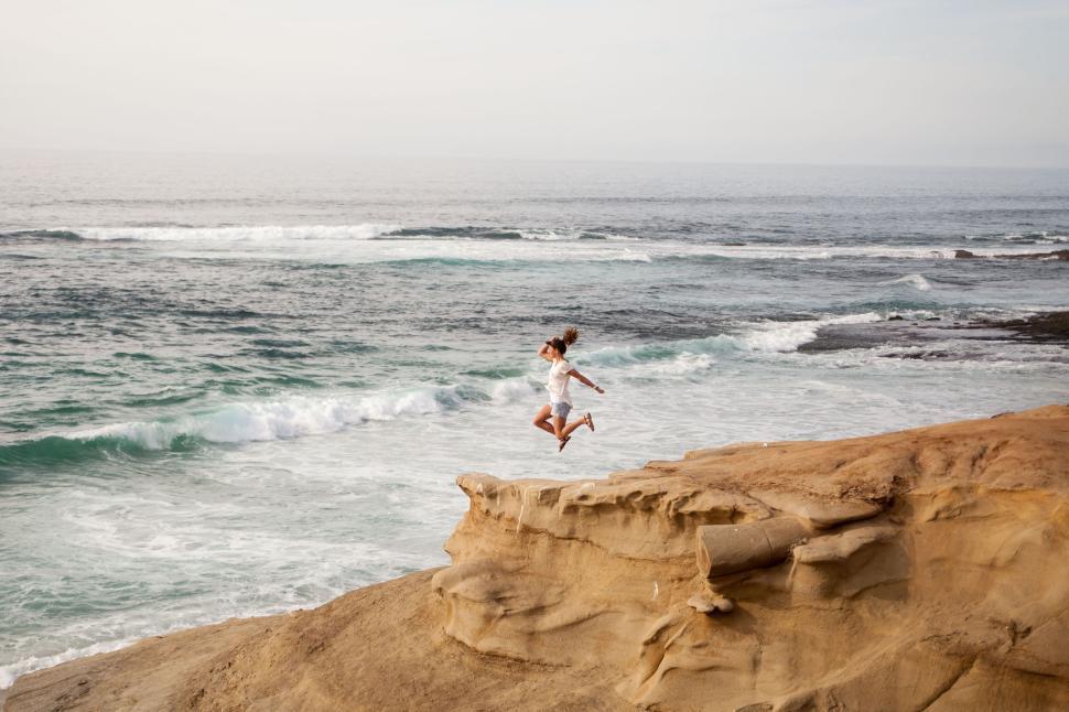 Free Image of Person jumping off rock cliff over ocean waves below. 