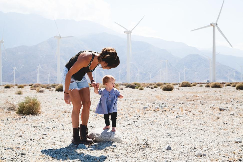 Free Image of Parent helping small child walk in desert wind farm. 