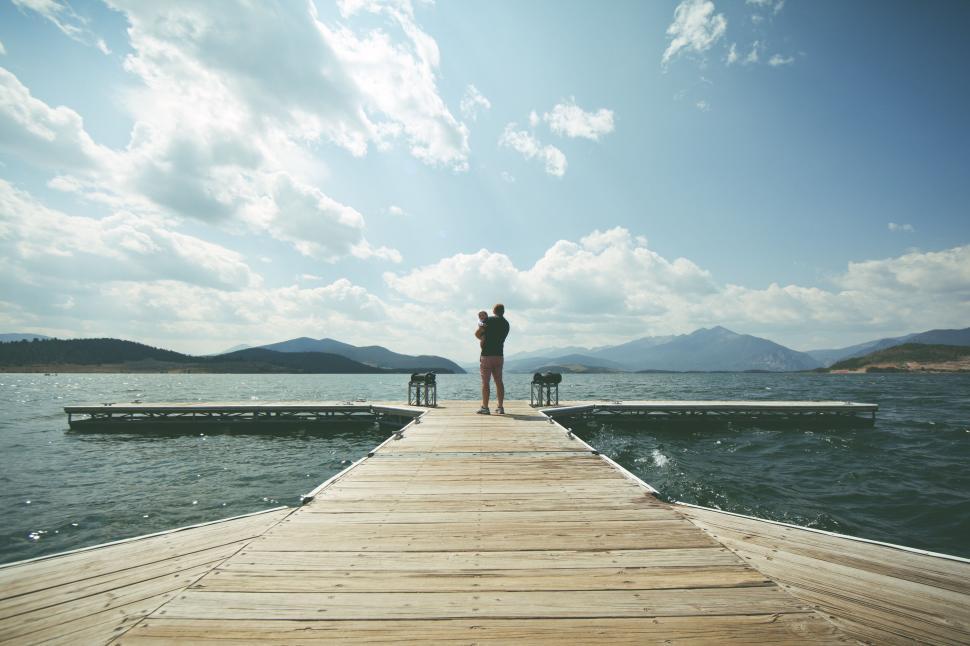 Free Image of Couple standing on dock overlooking a serene lake view 