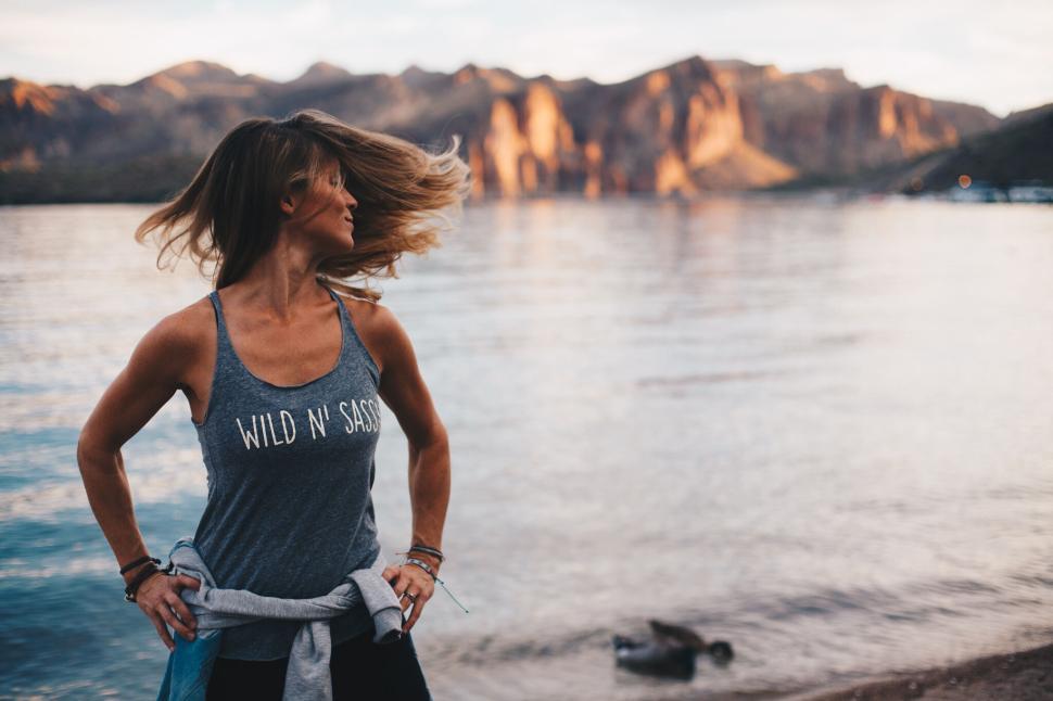 Free Image of Woman in tank top standing by serene mountain lake 