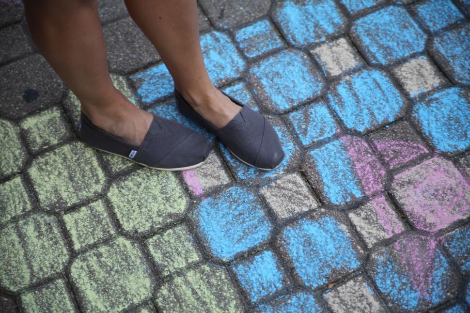 Free Image of Feet in shoes standing on colorful chalk pavement art 