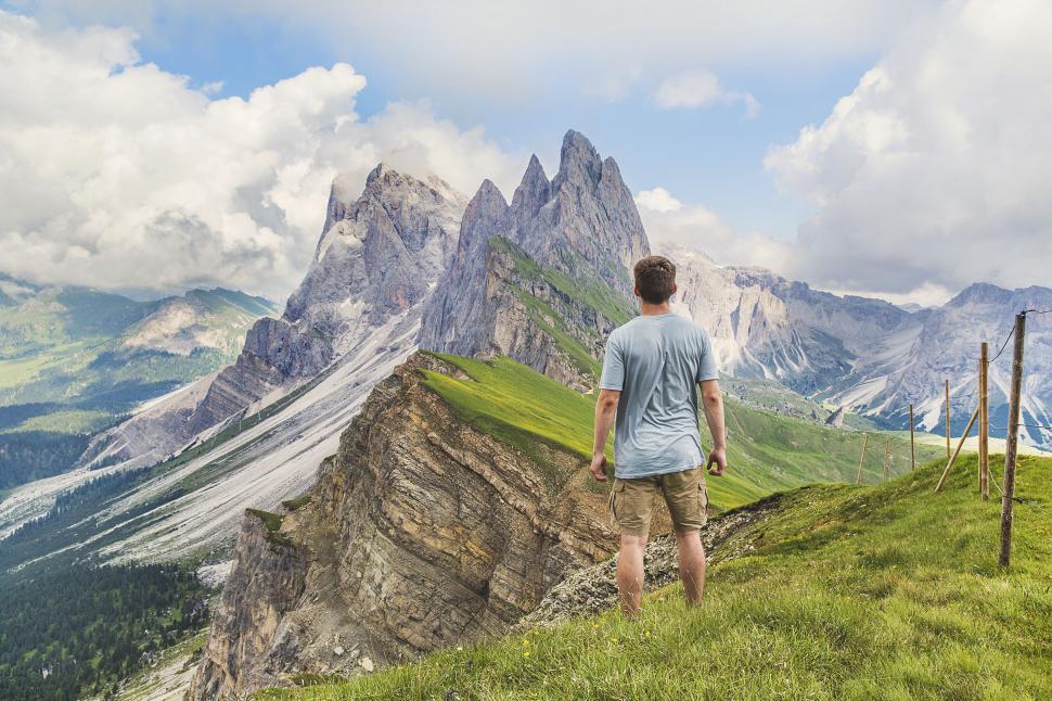 Free Image of Man on grassy ridge looking at sharp mountain peaks 