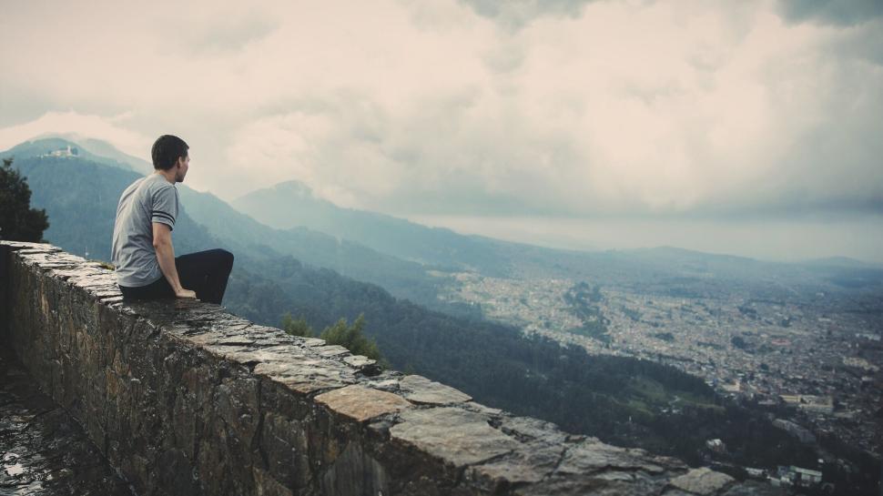 Free Image of Person sitting on a stone wall with a view of the city. 