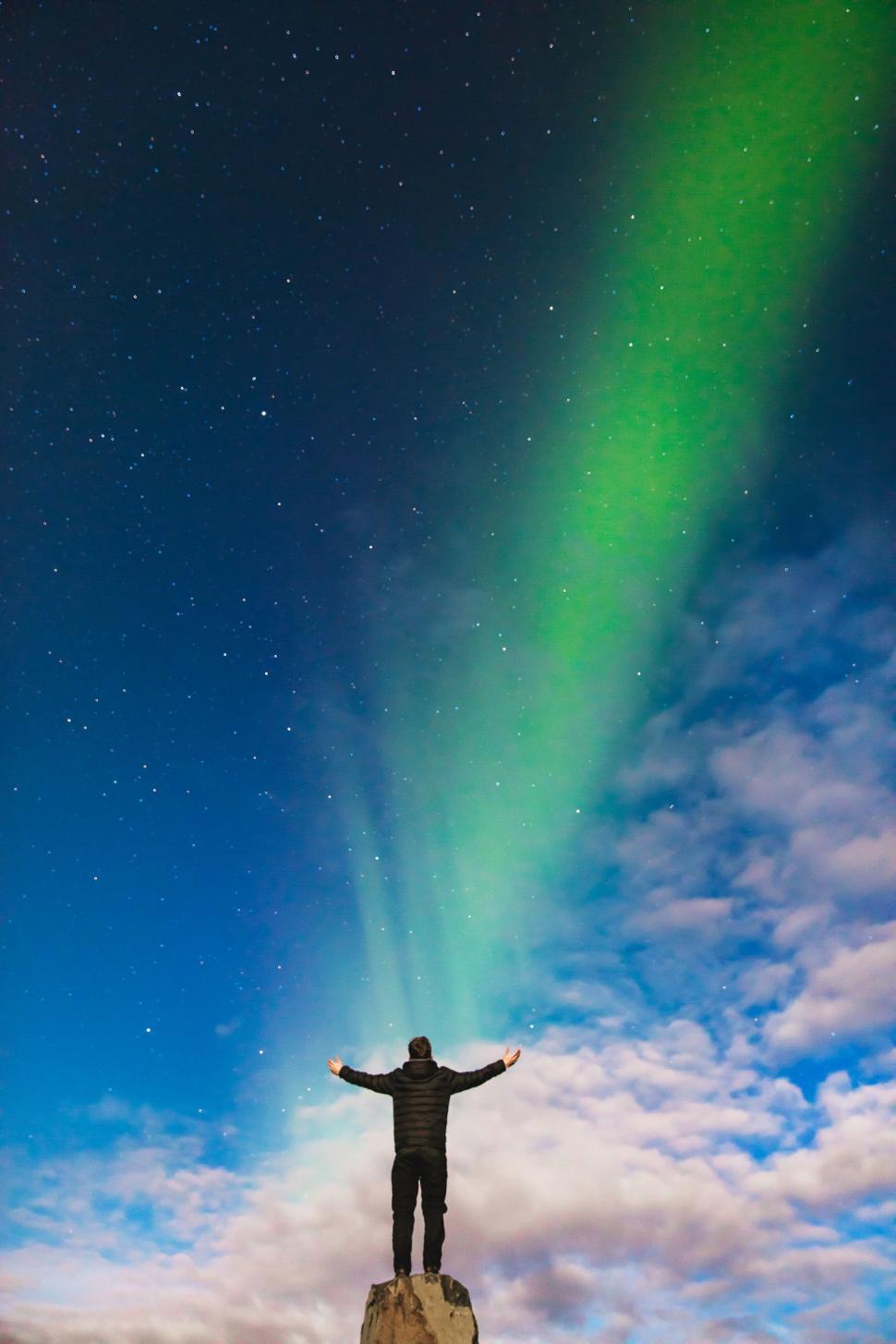 Free Image of Person standing under aurora borealis with arms raised 