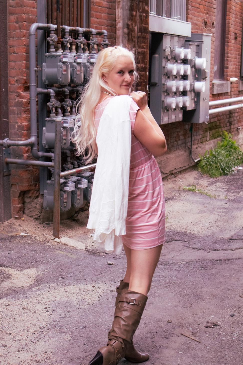 Free Image of Blonde woman in light pink dress smiling in alleyway 